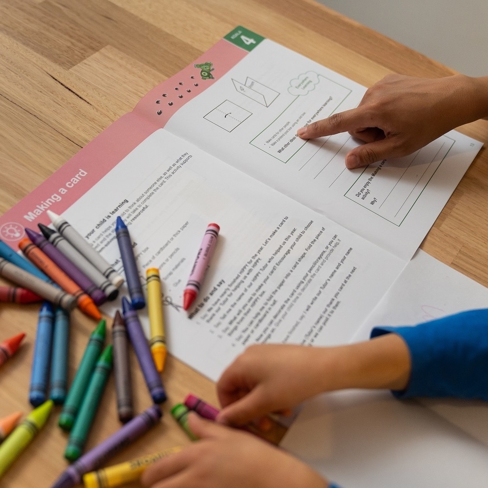 Child and carer completing a workbook page with crayons